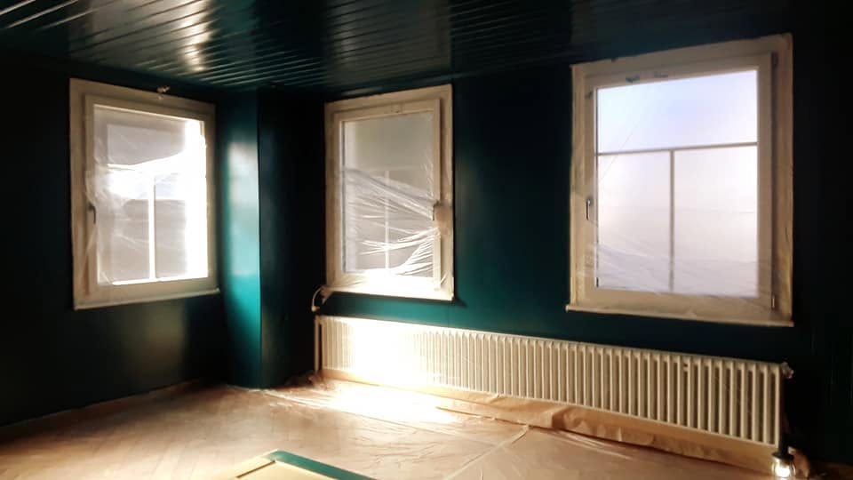 Malerarbeiten bei einer Innenrenovation: Wände und Täfer gestrichen, Boden und Fenster geschützt.